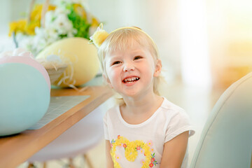 A little girl in the kitchen at a table by huge Easter eggs. Kids on Easter egg hunt.