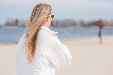 Woman in white jacket, sunglasses and blue jeans at the beach, new collection, fashionable trend