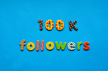 text 100 k followers  from bright colored paper letters on blue paper background