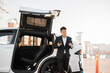 © sofiko14 - Focused asian man in business suit standing near charging electric car and using smartphone with bank card for paying online. Modern technology for urban lifestyles.
