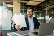 © Prostock-studio - Happy male entrepreneur reading business papers and smiling, checking company growth rates, sitting at desk in office