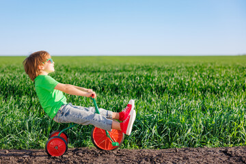 Canvas Print - Happy child riding bike outdoor in spring green field