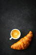 Croissant and cup of coffee at black background. Top view with copy space, vertical image.