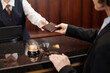 © pressmaster - Close-up of young reception staff in uniform taking passport of female guest passing it over check-in counter for registration in hotel