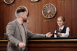 © pressmaster - Young female receptionist standing by counter in lounge and looking at male client while passing him passport after checking it in