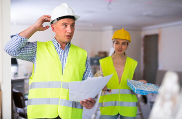 Wall Mural - Portrait of thoughtful man engineer holding project documentation. Woman painter standing in background. Renovation works in apartment.