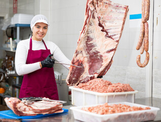 Young woman butcher in uniform hangs beef ribs on hook