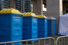 Row of portable plastic blue washrooms toilets on a city street set up for an outdoor event.