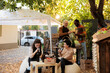 © DC Studio - Female client sitting at table with local winemaker tasting homemade natural wine, enjoying product sampling before purchasing produce. Shopping at organic street food festival farmers market.