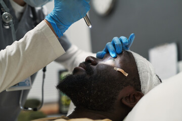 Wall Mural - Close-up of doctor or nurse opening eye of injured patient while directing light there while checking pupil reaction during examination