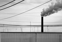A Contrasty, Black And White Image Of Pollution From A Smokestack Framed In Power Lines In An Industrial City 