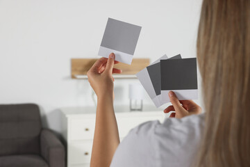 Poster - Woman choosing paint shade for wall in room, focus on hands with color sample cards. Interior design