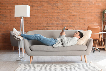 Poster - Young man using tablet computer on grey sofa at home