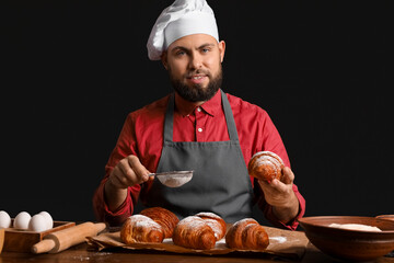 Canvas Print - Male baker sprinkling croissants with sugar powder at table on dark background