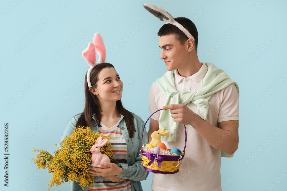 Happy young couple with Easter eggs, rabbits and mimosa flowers on blue background