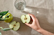 Hand holding half of green apple. Fresh fruits and glass of water on table, healthy nutrition concept