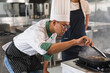 Portrait Asia young man in chef uniform cooking steak fire with student woman assistance chef at kitchen	