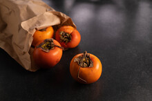 Persimmon Fruits In A Paper Bag On A Dark Background, Place For Text