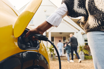 Wall Mural - Woman plugging electric charger into car outside Home With Family