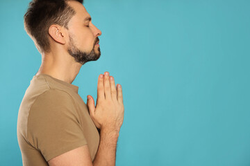 Wall Mural - Man with clasped hands praying on turquoise background. Space for text