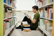 © DragonImages - College student sitting on library floor and working on project