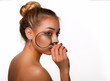 © oleg_ermak - Beautiful face youth and skin care concept. Young woman with clean skin, blond hair tied in knot and blue eyes holds near the face magnifying glass on white background in hard shadow lighting.