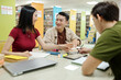 © DragonImages - Joyful college students discussing ideas for project at table in library