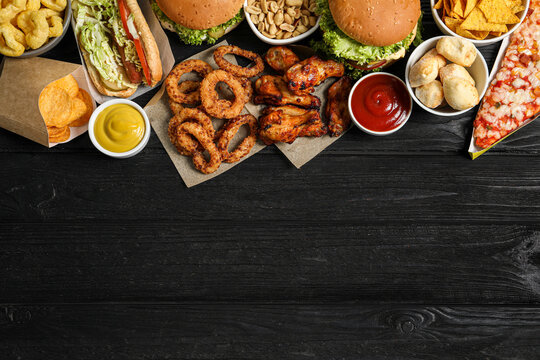 Wall Mural - Burgers, onion rings and other fast food on black wooden table, flat lay with space for text