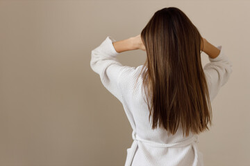 Wall Mural - Young woman with healthy long smooth hair in white bathrobe, rear view. Hygiene, freshness, cleansing after shower. Effect of cosmetic products for hair and body care. Healthy cosmetic hair care.