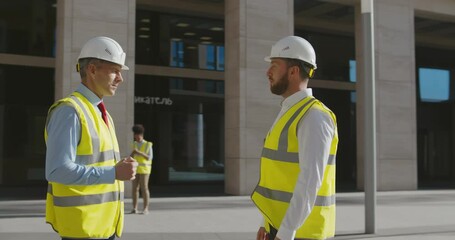 Wall Mural - Civil engineers wearing safety vest and helmet, shaking hands discussing project outside office