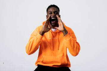 Photo of handsome african american man guy in orange hoodie and white t-shirt standing over grey background in studio isolated screaming yelling shouting while shooting process.