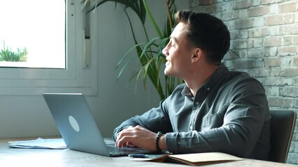 Wall Mural - Thoughtful businessman touching chin, pondering ideas or strategy, sitting at wooden work desk with laptop, freelancer working on online project, student preparing for exam at home
