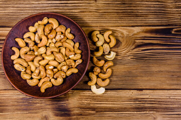 Poster - Ceramic plate with roasted cashew nuts on a wooden table. Top view