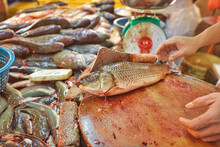 A Close-up Of A Fishmonger Cleaning The Fish At A Chow Kit Road Market Stall In Kuala Lumpur. It's A Busy Market With Shoppers Perusing The Stalls.