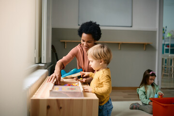 Wall Mural - Happy black teacher and little boy play with puzzles at kindergarten.