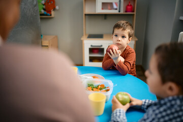 Wall Mural - Small boy eats an apple after lunch at preschool.