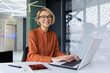 © Liubomir - Portrait of happy and successful female programmer inside office at workplace, worker smiling and looking at camera with laptop blonde businesswoman is satisfied with results of achievements at work