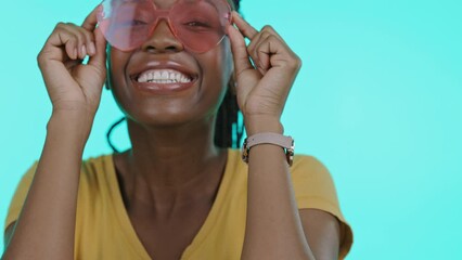 Wall Mural - Face, fashion and eyewear with a black woman winking in studio on a blue background to model sunglasses. Portrait, smile and style with an attractive young female indoor to promote a brand of shades