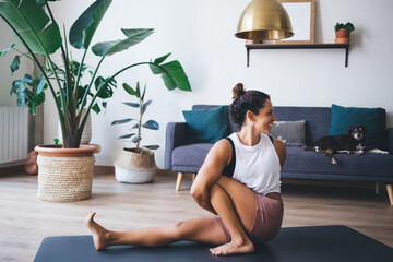 Wall Mural - Happy flexible female yogi enjoying stretching exercises on mat carpet, cheerful Caucasian woman warm up body muscles before pilates workout for mindfulness and harmony meditation in asana mantras