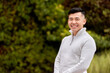© JoseIMartin - Asian man looking at the camera and smiling while standing outdoors in a park.