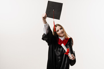 Graduate girl is graduating high school and celebrating academic achievement. Masters degree diploma in hands. Happy student in black graduation gown and cap is smiling on white background.