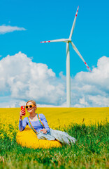 Sticker - Beautiful female in rainbow LGBT suspenders for pants and mobile phone is sitting in bean chair in rapeseed field