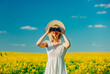 Beautiful woman in dress with binoculars in rapeseed field