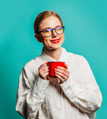 Poster - Portrait of beautiful blonde in white shirt with cup of coffee on blue background