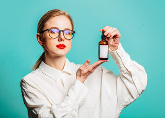 Canvas Print - Portrait of beautiful blonde in white shirt with cosmetic bottle on blue background