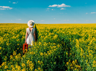 Sticker - Beautiful woman in dress with suitcase in rapeseed field in spring time