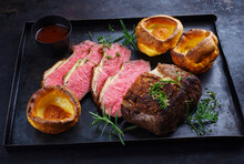 Traditional Commonwealth Sunday Roast Beef Sliced With Yorkshire Pudding And Red Wine Sauce Served As Close-up On A Rustic Black Metal Tray