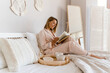 © mary_markevich - pretty smiling woman relaxing at home on bed in morning in pajamas reading book
