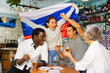 Emotional multiracial spots supporters with flag of Russia happy about victory in championship in pub