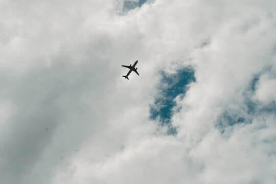 silueta y vista desde abajo del paso de un avión comercial con muchas nubes y cielo azul.